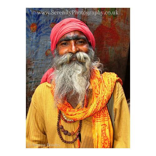 An Indian holy man with a long grey beard poses for a photo. Varanasi, India.